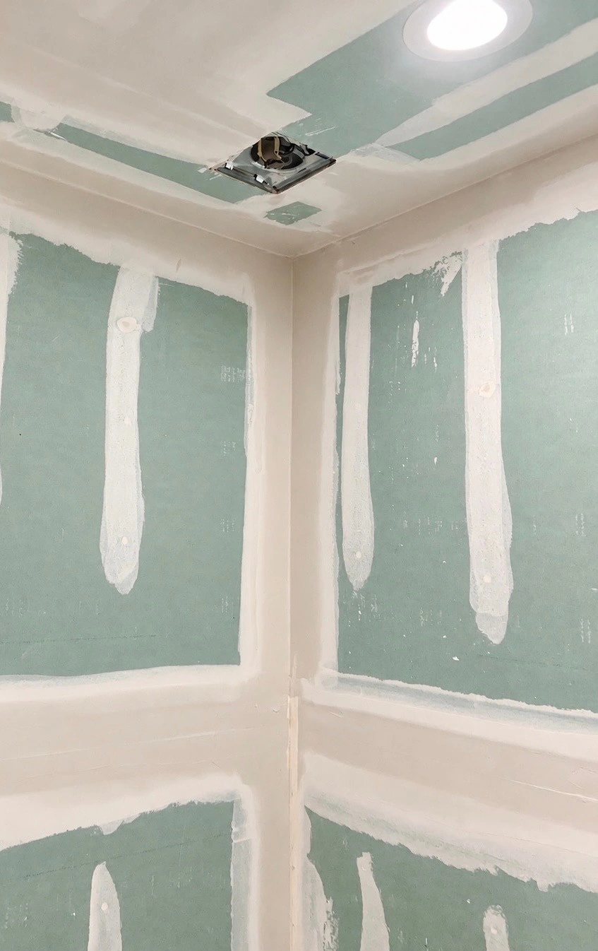 Joint compound on green drywall boards, corners, and a ceiling